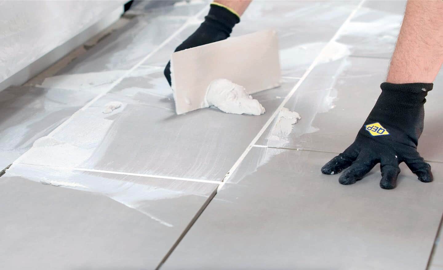A person applying grout to floor tile.