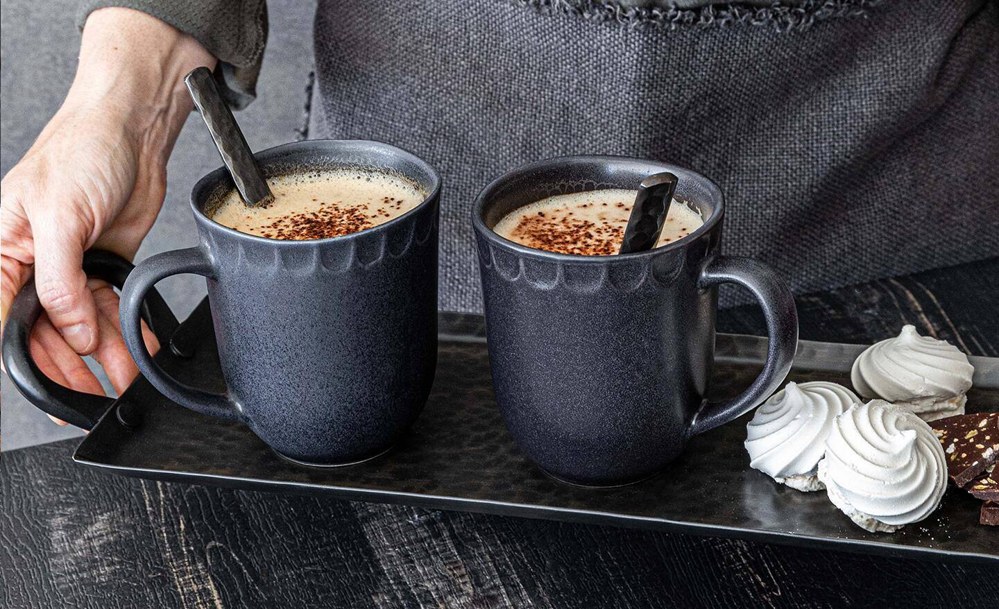 A person holds a tray with two stoneware mugs on it. A person holds a tray with two stoneware mugs on it.