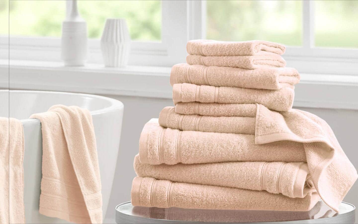 Stacked beige towels in different sizes, with others hung on a towel rack. Stacked beige towels in different sizes, with others hung on a towel rack.