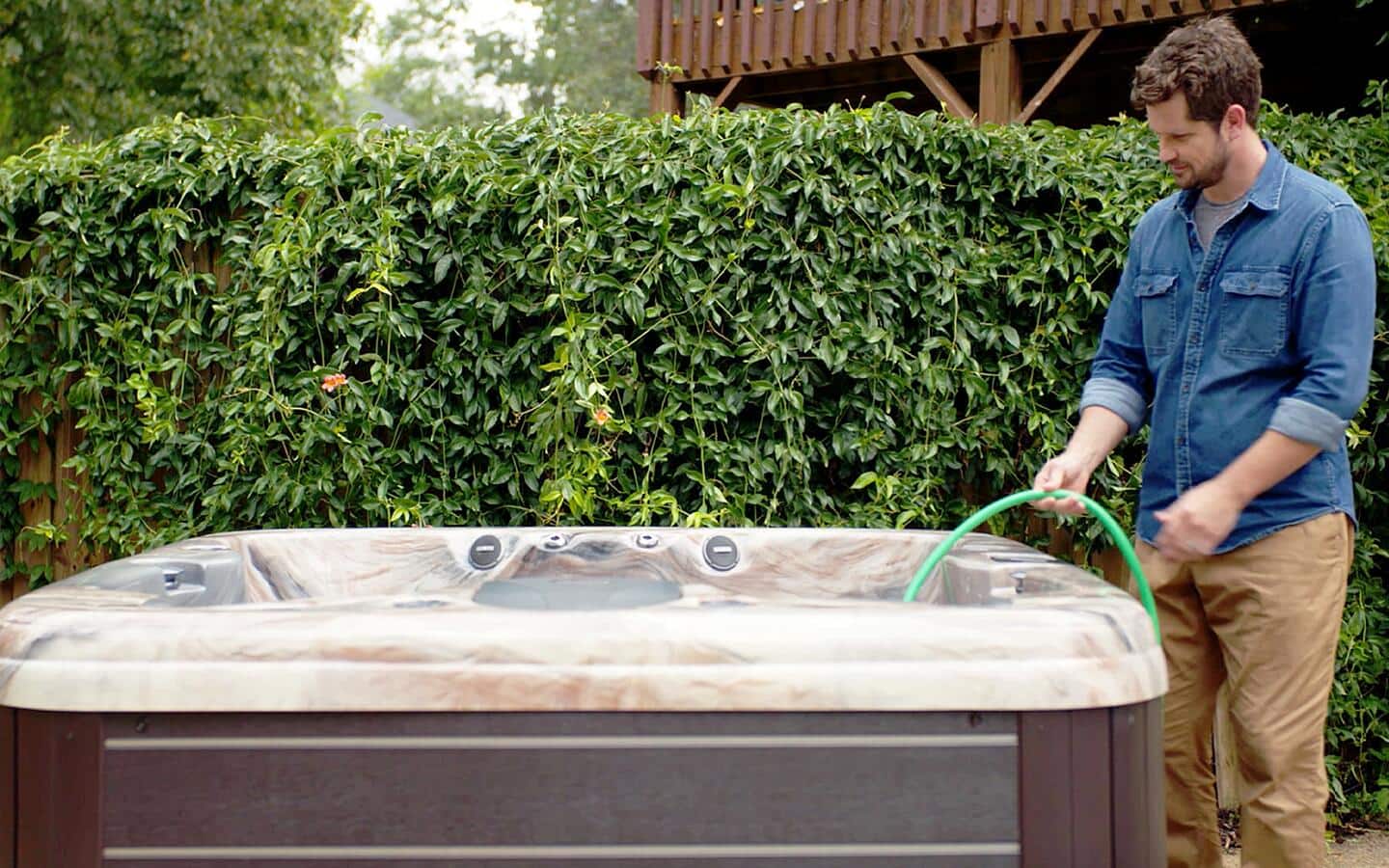A person filling a hot tub with a hose.