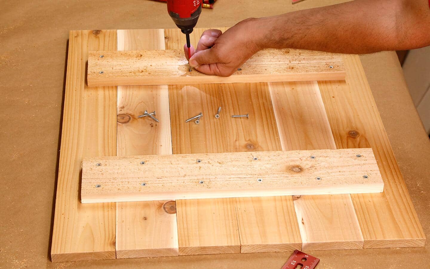 An individual driving screws into the lid for a wooden bin.