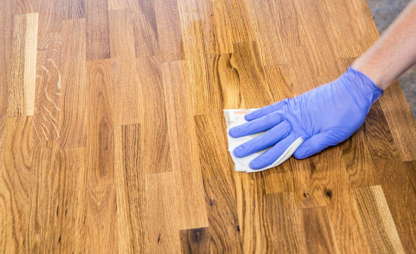 A person uses a cloth to clean a butcher block countertop surface.