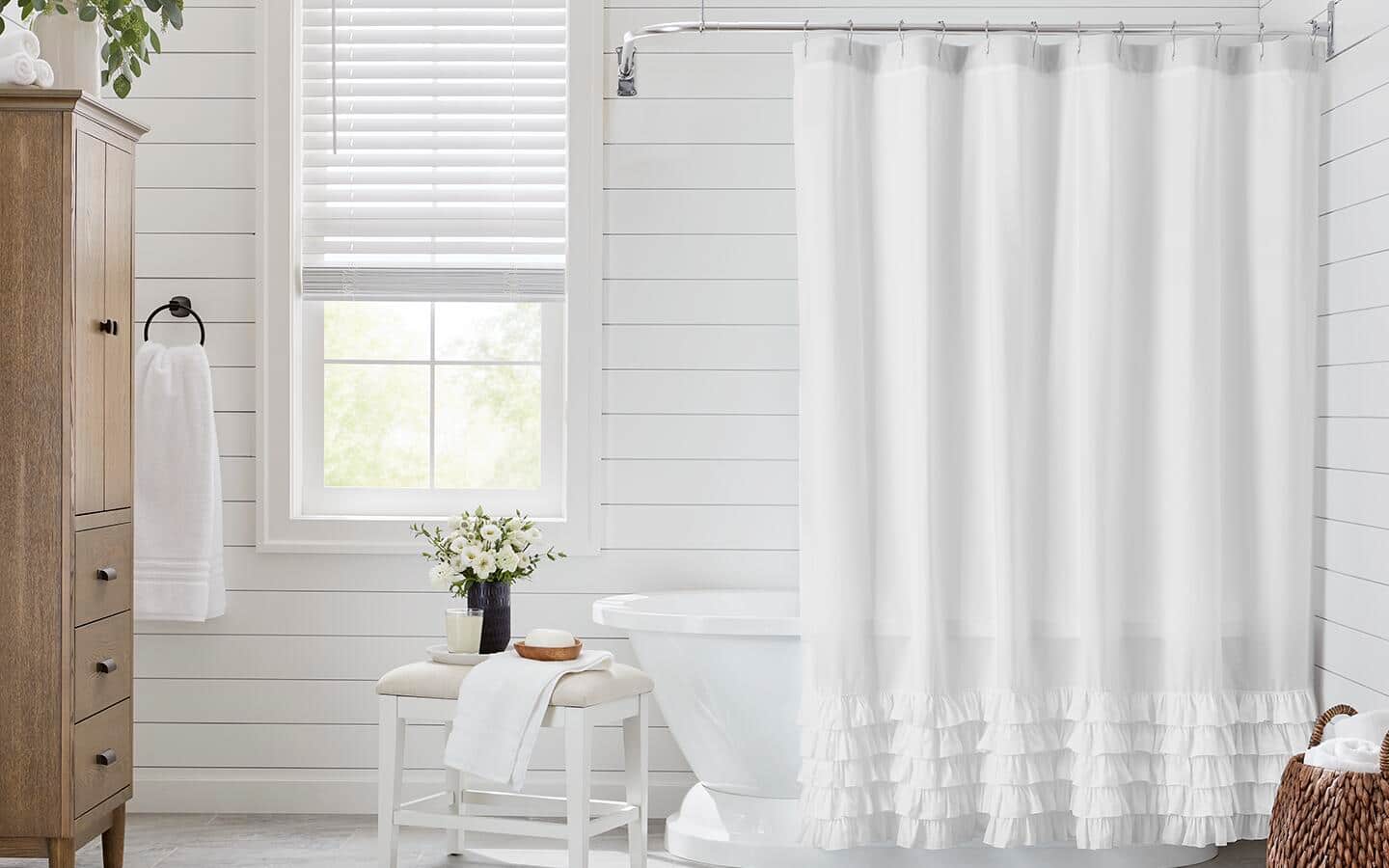 A neutral shower curtain surrounding a tub next to a wooden chest.
