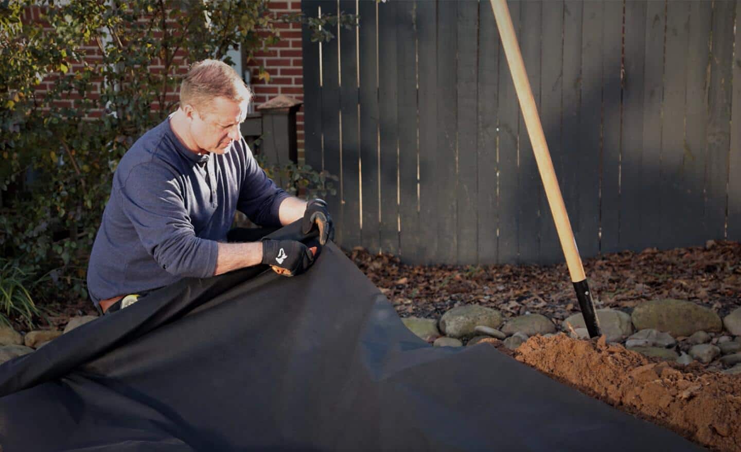 A person lines a French drain trench with filter fabric.