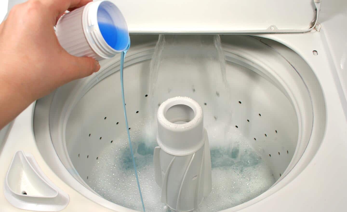 Someone pouring detergent into a top load washer.