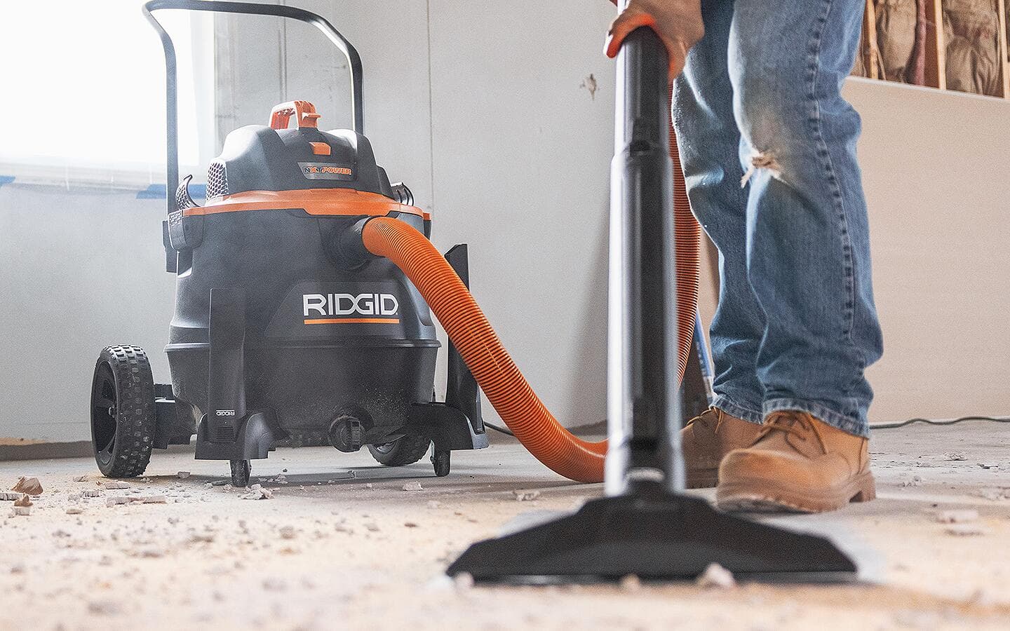 A person uses a shop vac to clean sawdust and debris from a floor.