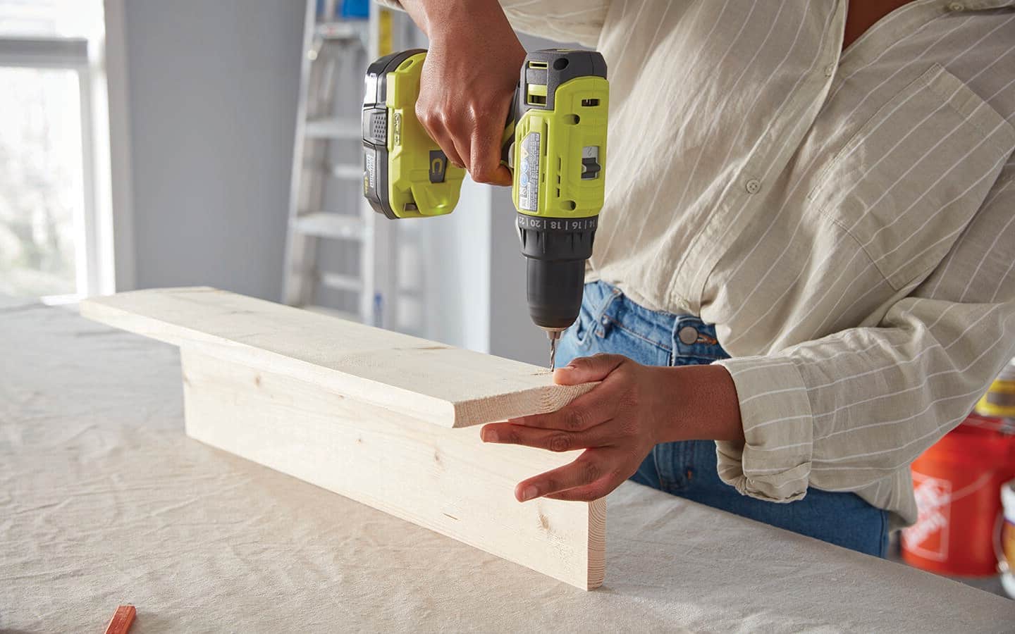 A person uses a drill to create mounting holes in the pipe coat hanger.