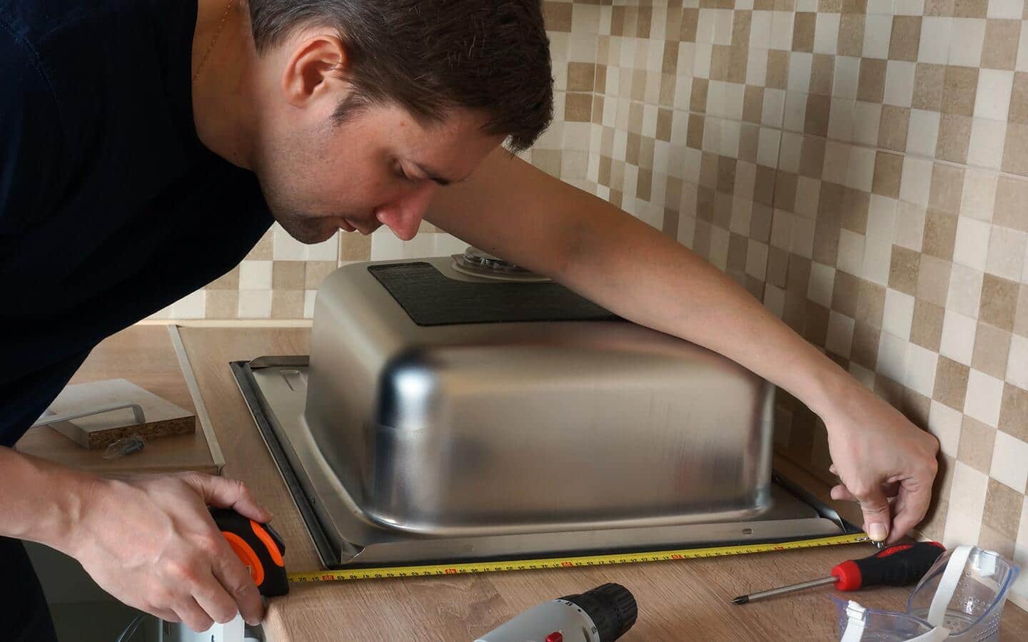 A person in a black t-shirt measuring a kitchen sink on a countertop. A person in a black t-shirt measuring a kitchen sink on a countertop.