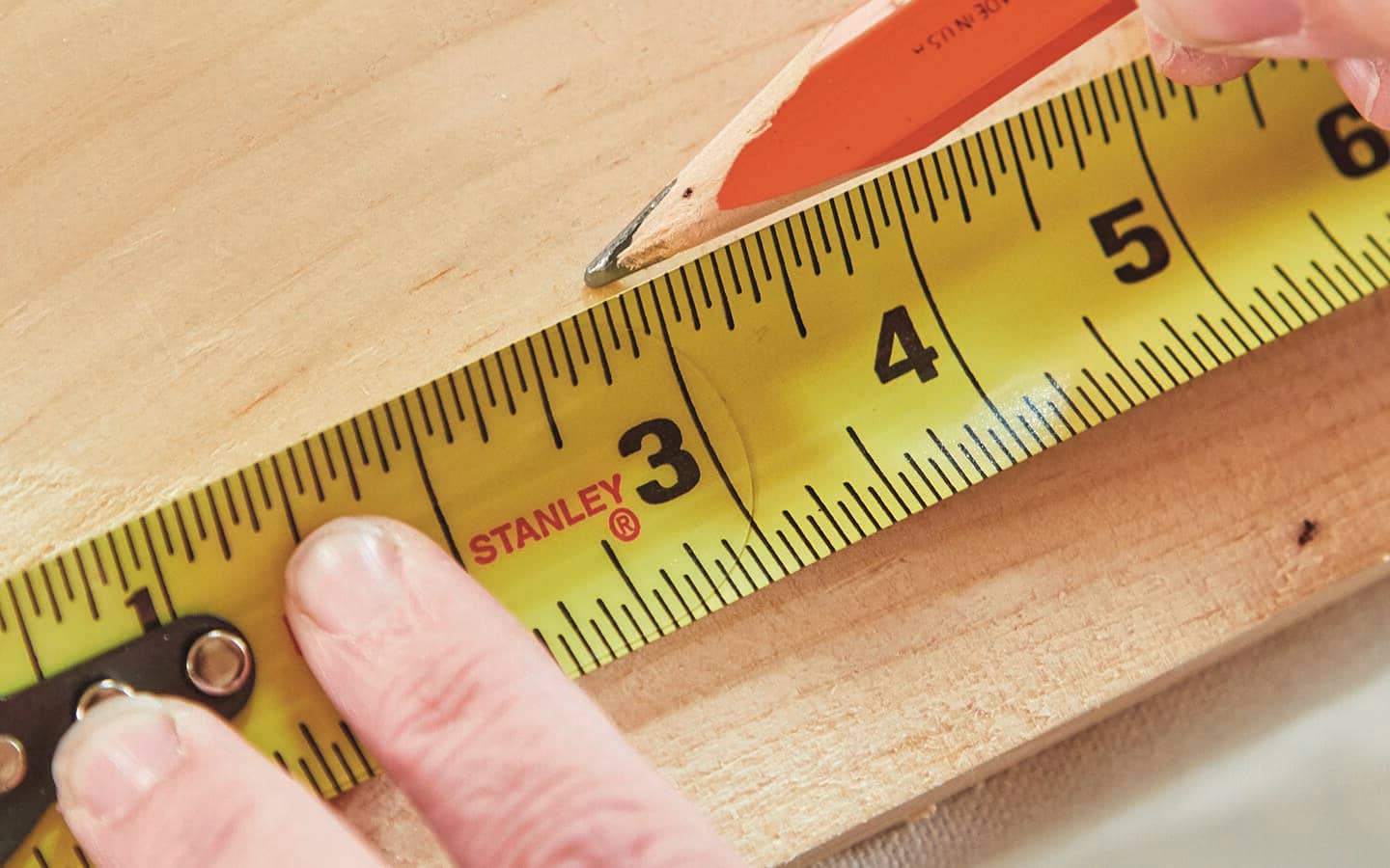 A person uses a tape measure and pencil to mark wood for a sofa table.