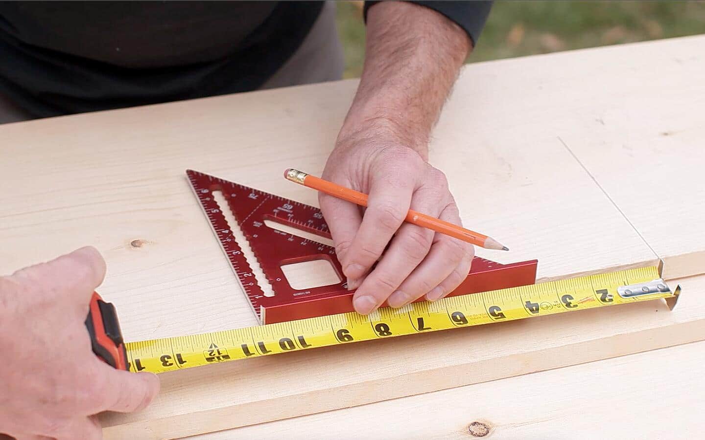 Someone measuring a wooden board with a pencil, tape measure and carpenter's square. 