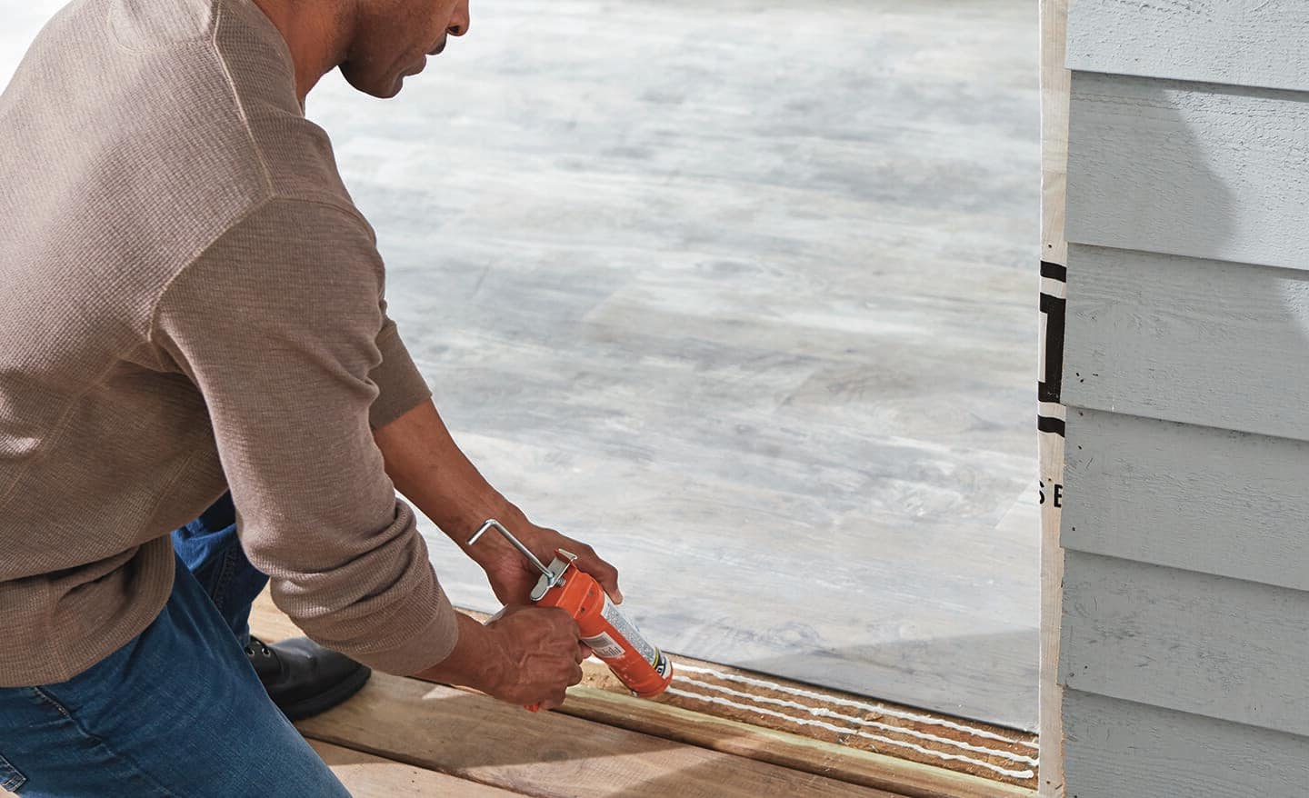 A man caulks the bottom opening of a frame for sliding door installation.