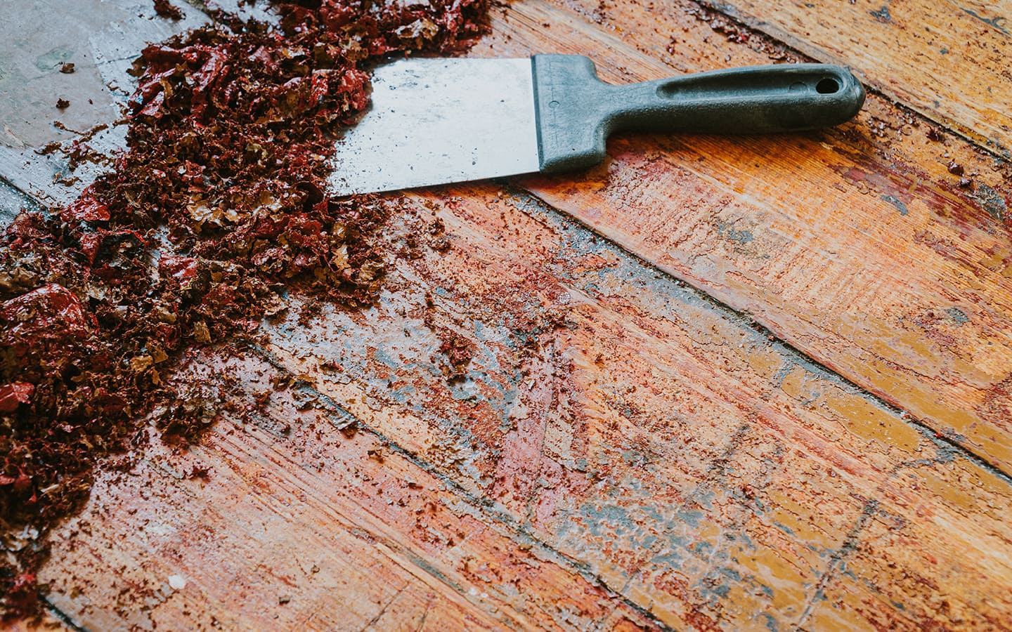 A putty knife and scraped debris on a wood deck