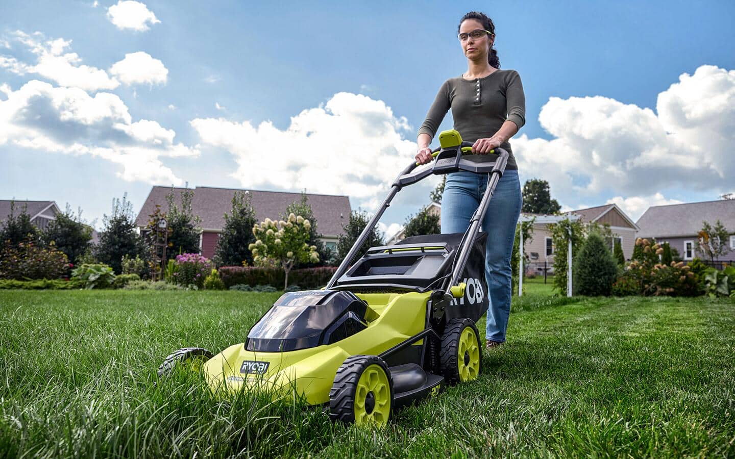A person uses a lime green push mower in their front yard. A person uses a lime green push mower in their front yard.