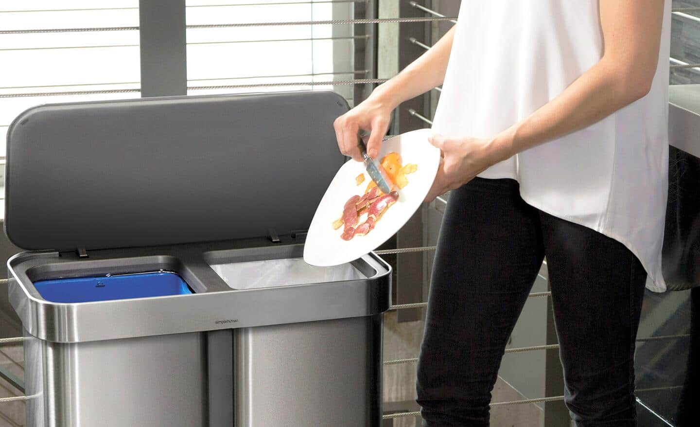 Someone putting food in a kitchen trash can.