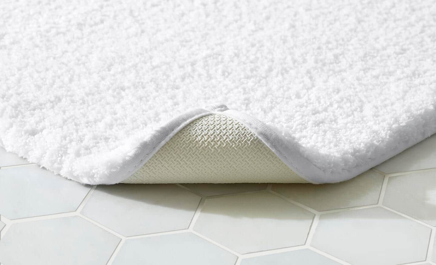 A white bath mat flipped back to show its slip-resistant side.