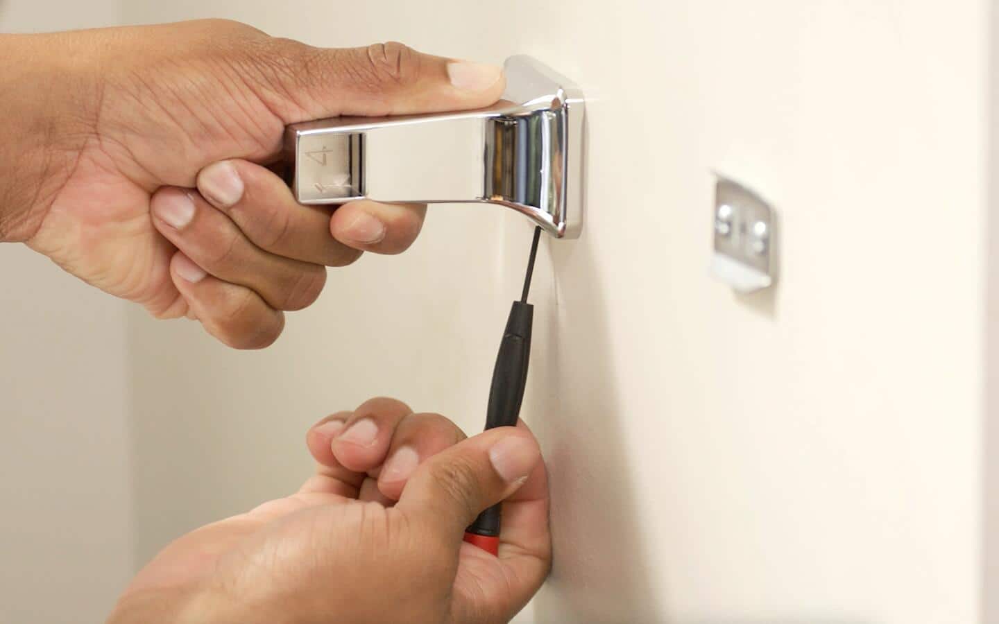 A person secures the bottom screw into a toilet paper holder.