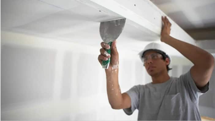 A Pro installs drywall on a ceiling.