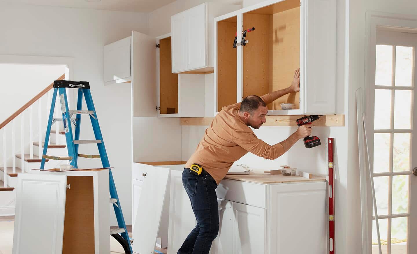 A person drills screws while attaching doors to cabinets.