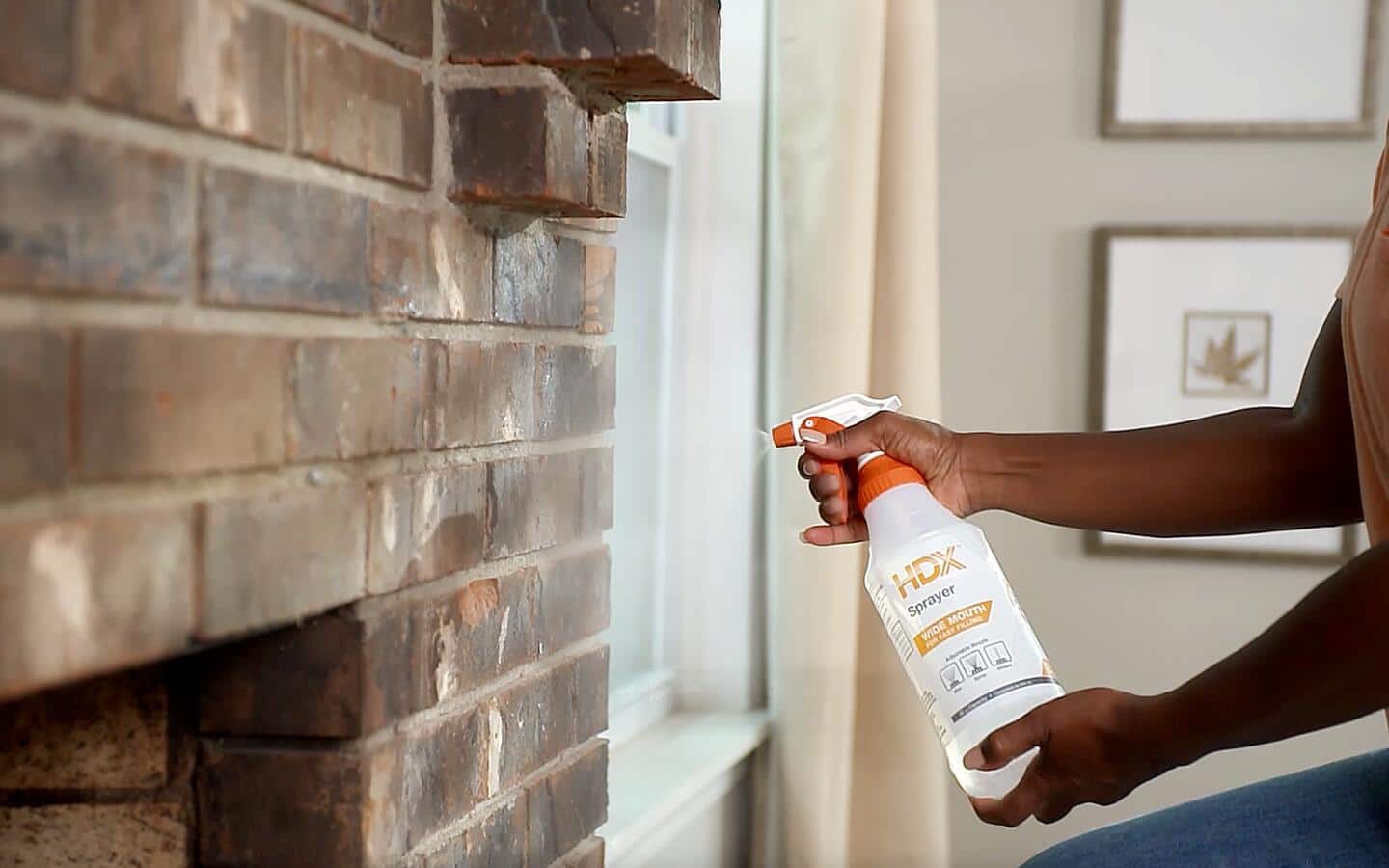 A person sprays a cleaning solution to a brick fireplace wall.