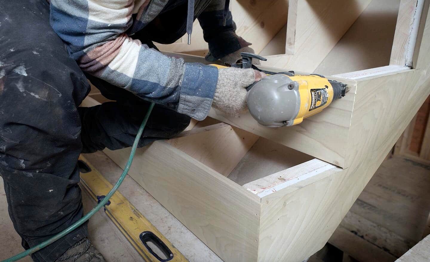 A worker fastens stair riser boards into place with a pneumatic nail gun.