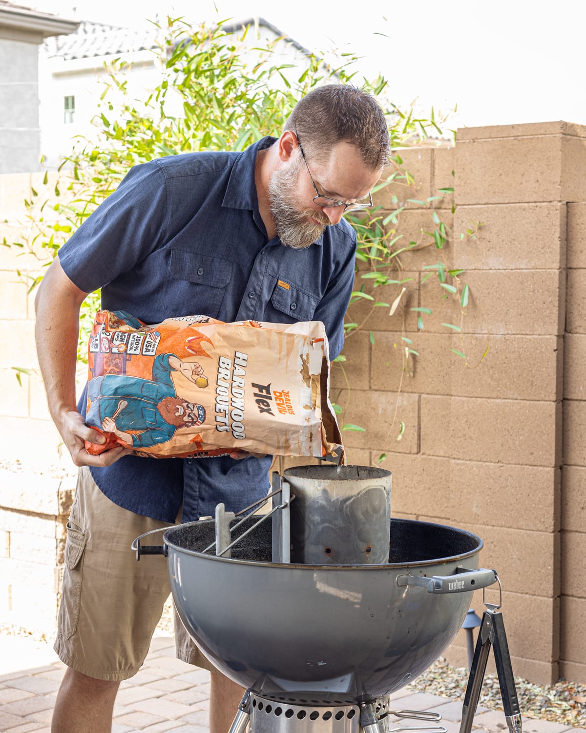 A man pouring briquettes into a chimney charcoal starter over a grill. A man pouring briquettes into a chimney charcoal starter over a grill.