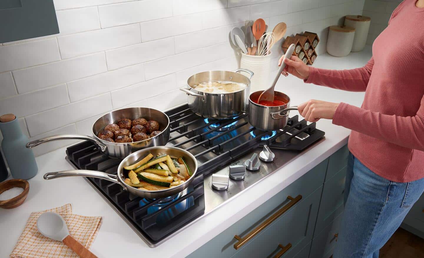 A person using four pots to cook on top of a stovetop 