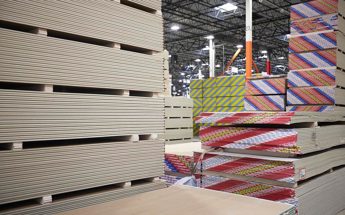 Multiple stacks of drywall stored in an illuminated warehouse. Multiple stacks of drywall stored in an illuminated warehouse.
