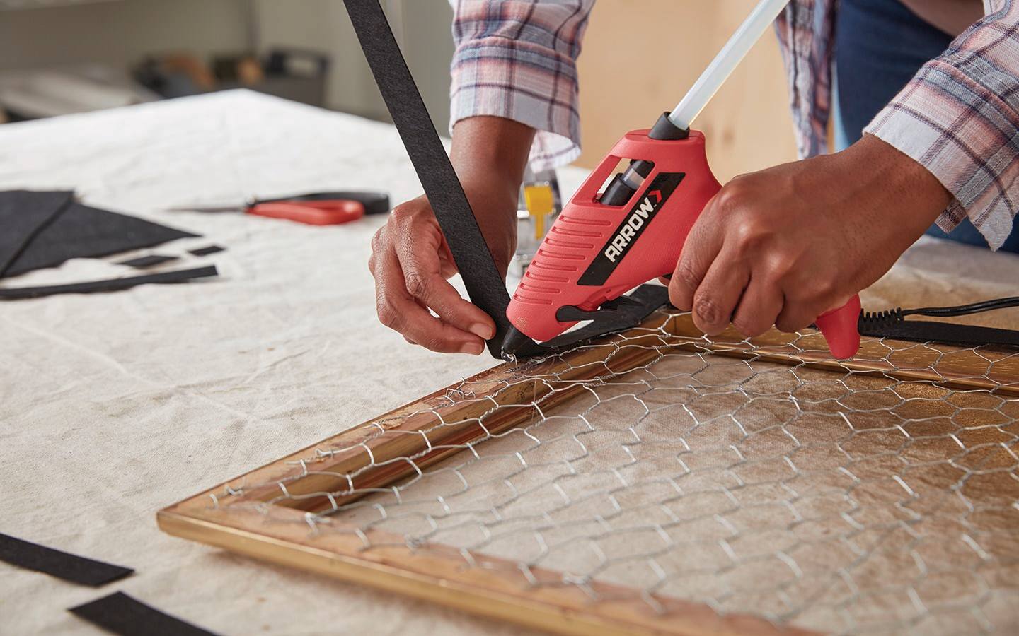 A person uses a glue gun to attach backing to a frame. A person uses a glue gun to attach backing to a frame.