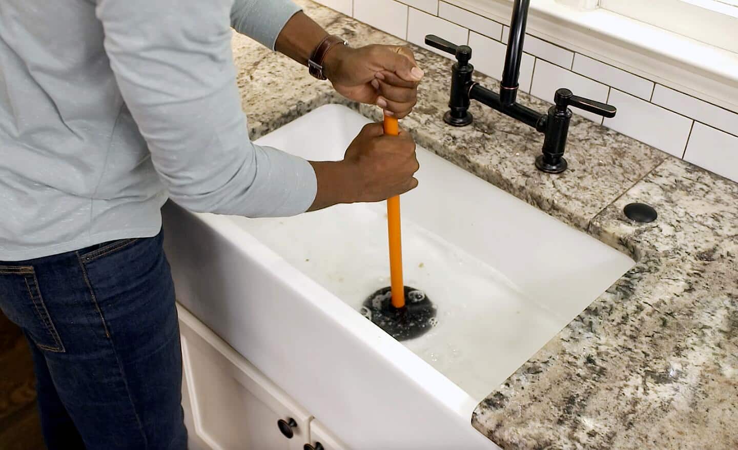 A person trying to unclog a sink using a plunger.