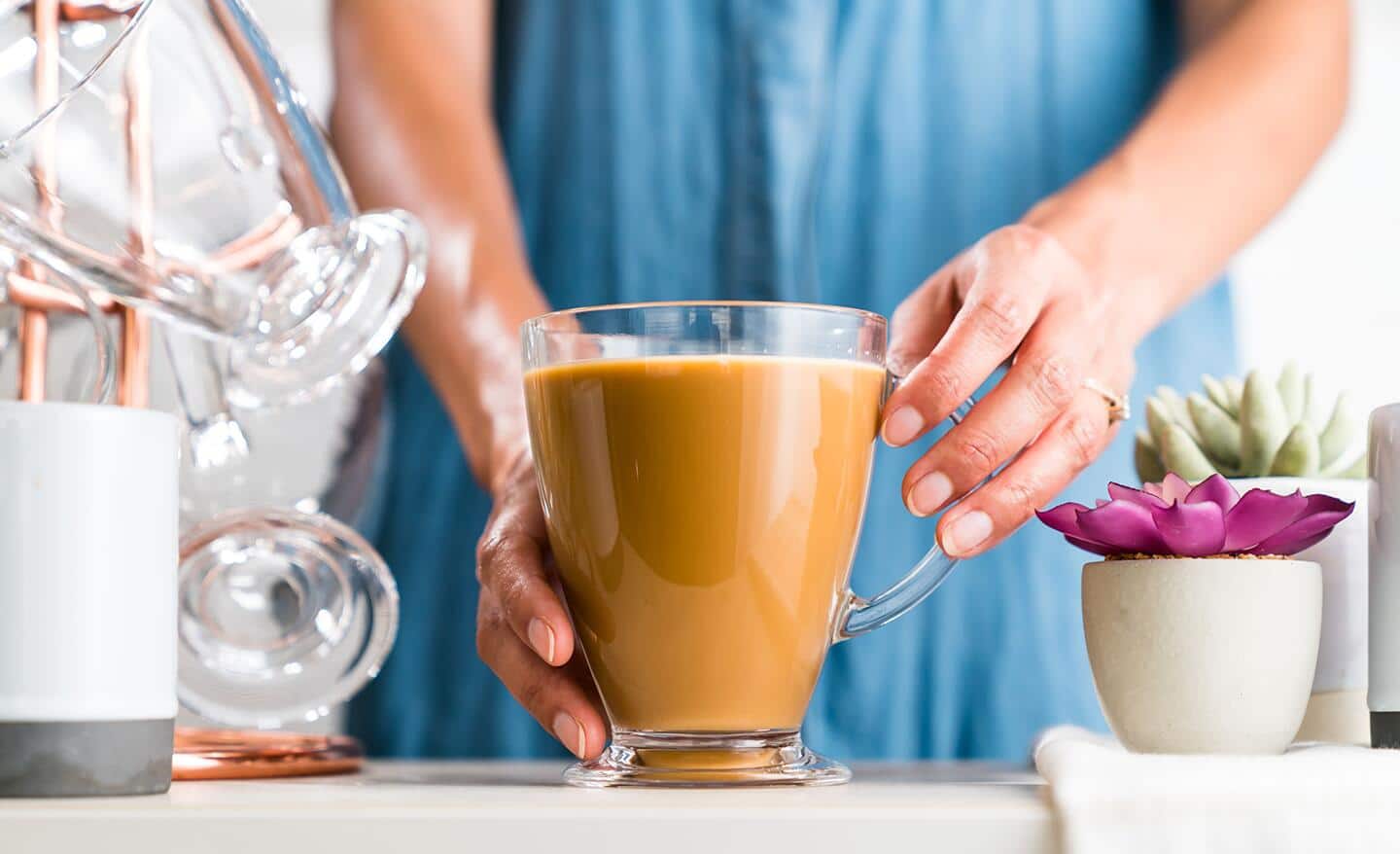A woman wearing a blue dress holds a glass mug full of coffee. A woman wearing a blue dress holds a glass mug full of coffee.