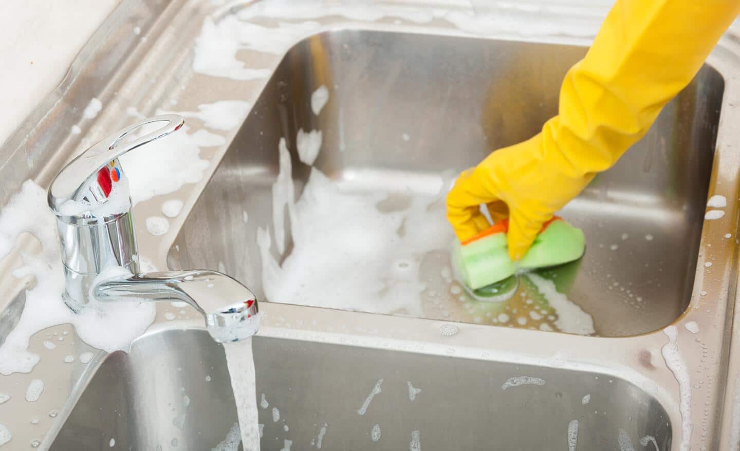 A person scrubs a kitchen sink with a sponge.
