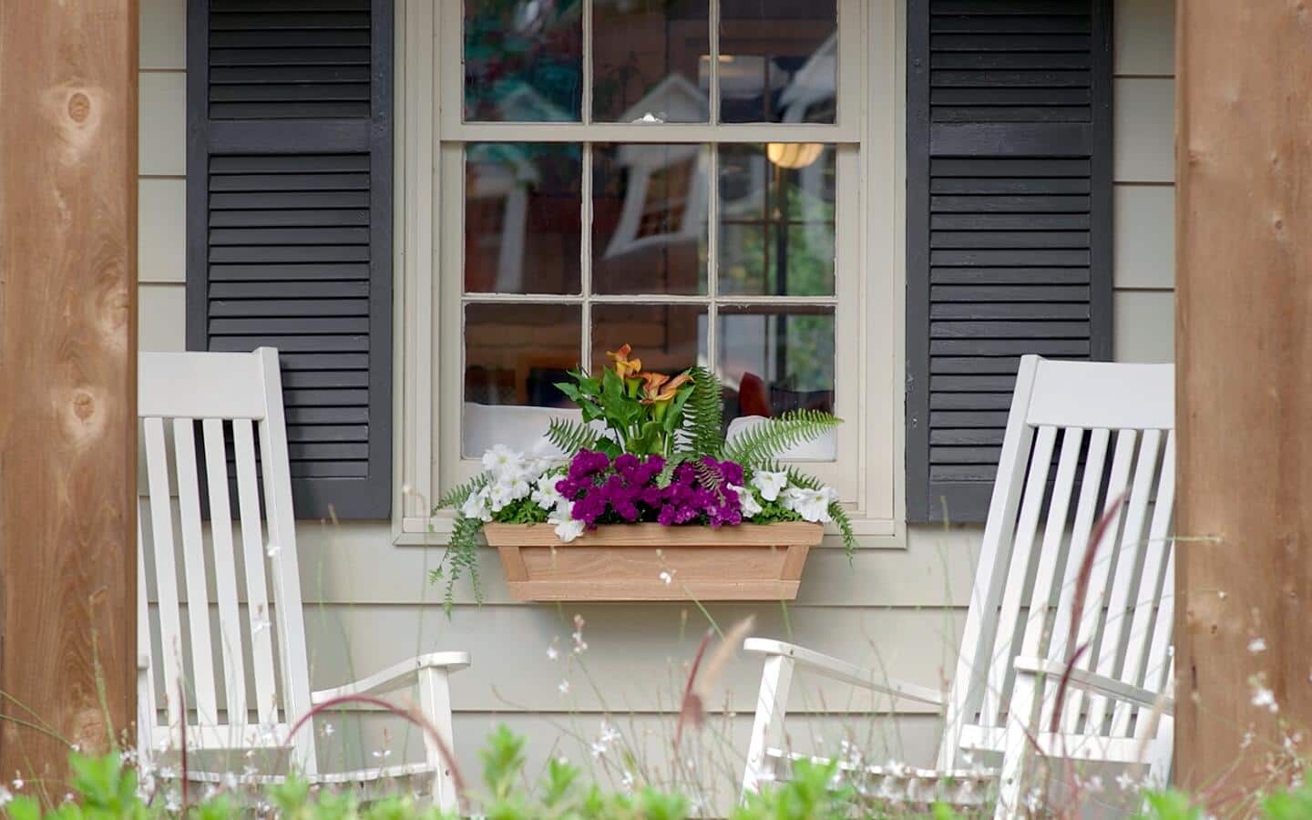 A finished window box with multiple flowers located underneath a window.