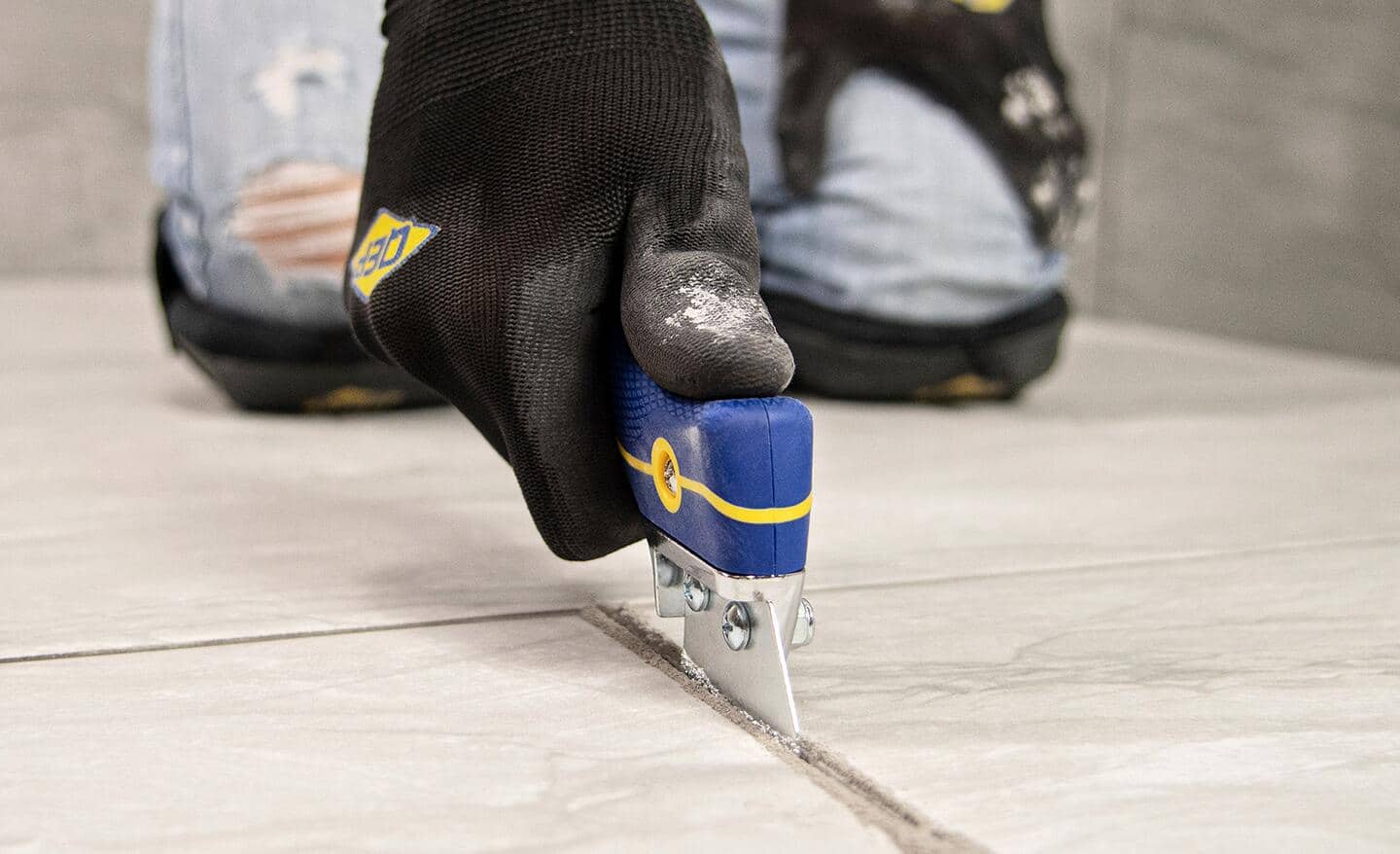 Person uses a grout saw to remove grout between tiles