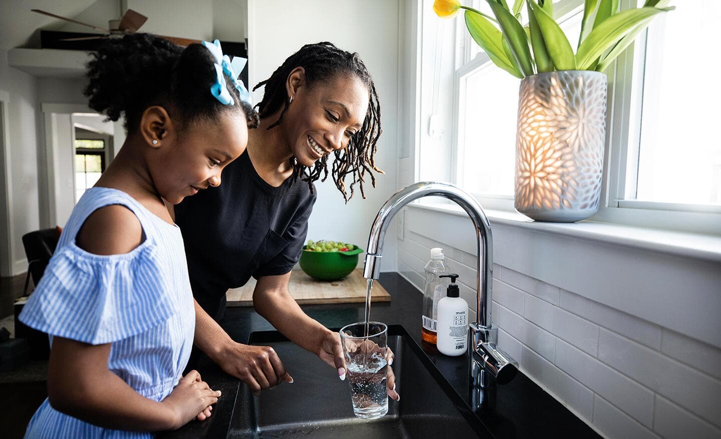 A mother and daughter fill a glass of water from the tap.
