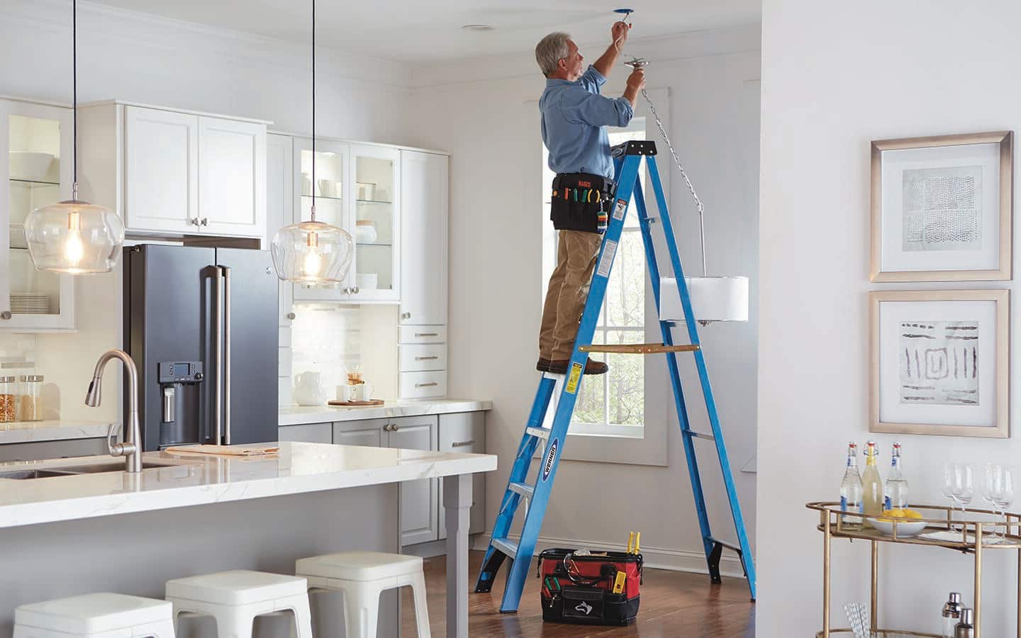 A man uses a tall stepladder to reach an electrical box in a ceiling.