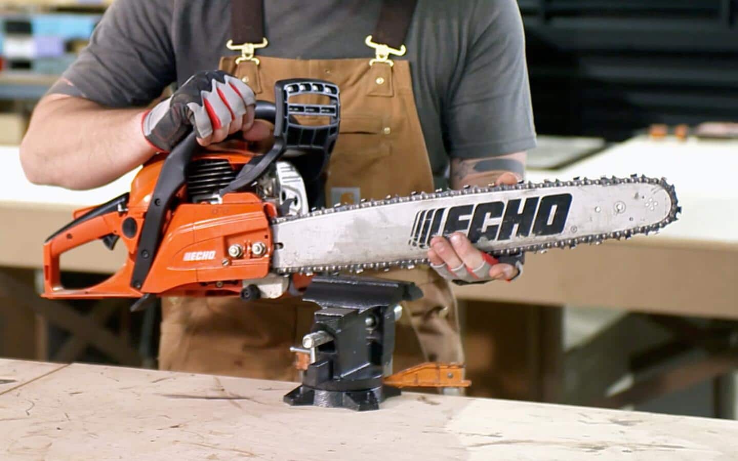 A person places a chainsaw in a vise to secure it on a workbench. A person places a chainsaw in a vise to secure it on a workbench.