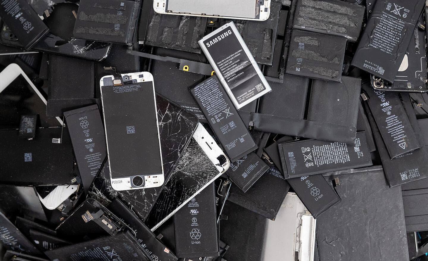 Old and broken laptop batteries, cell phone batteries and phones in a pile.