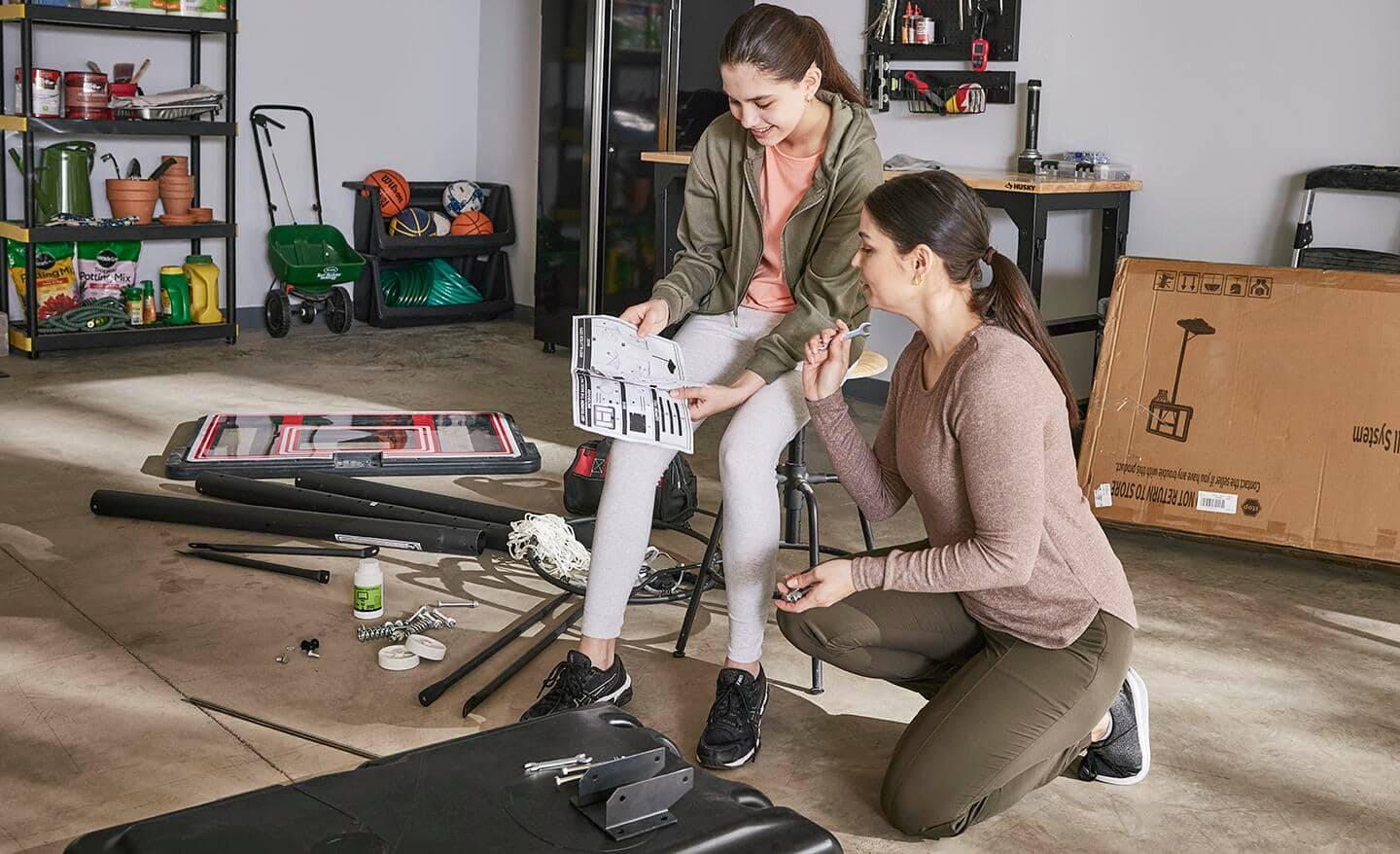 Mom and daughter in garage sorting through parts for a portable basketball hoop.