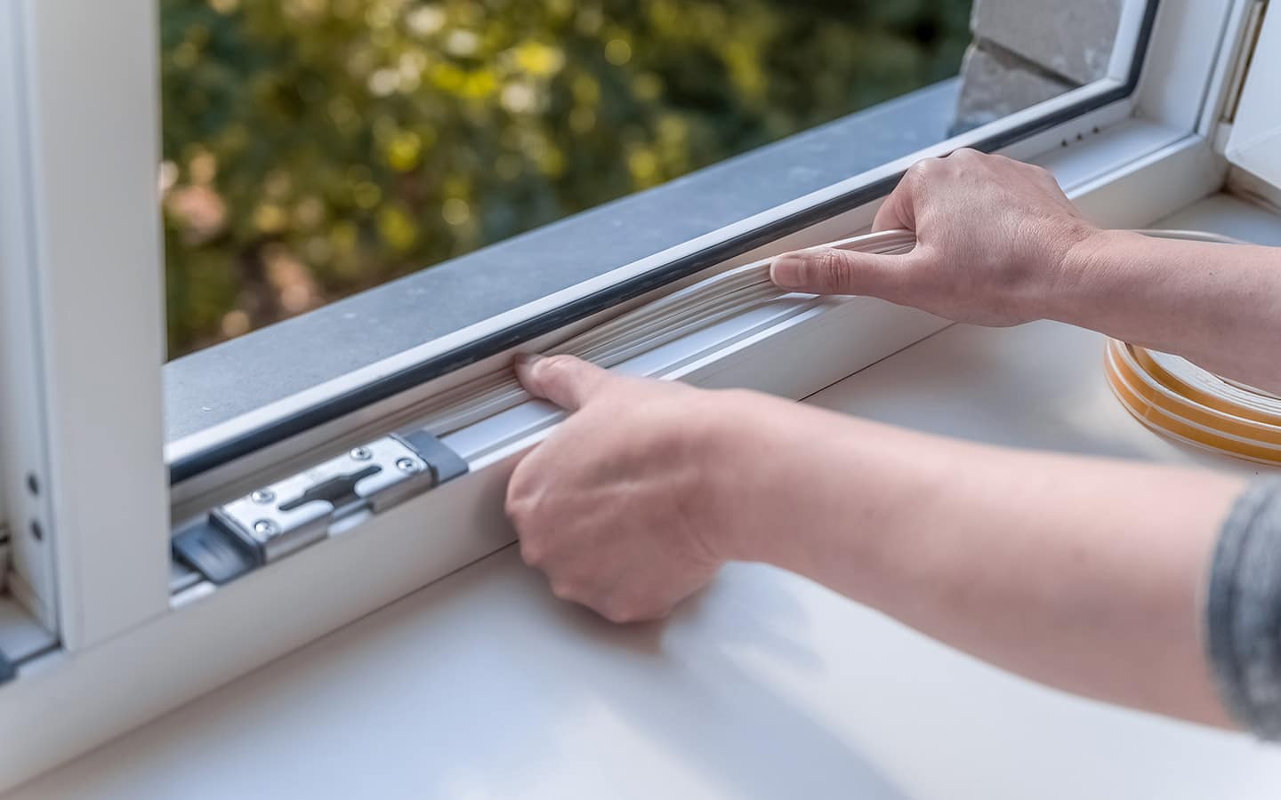 Someone adding weatherproofing to a white window frame.