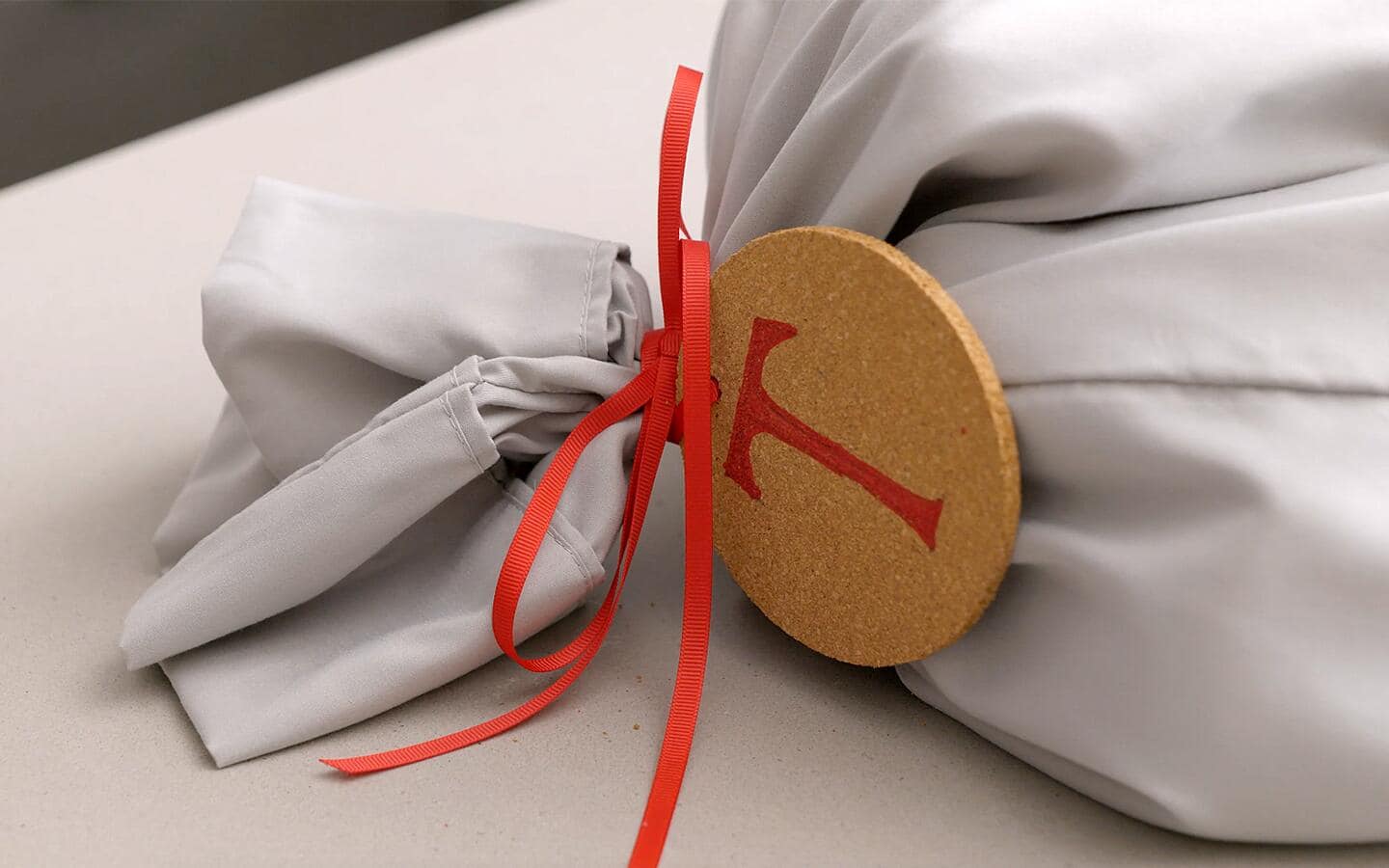 A gray pillowcase is tied shut with a red ribbon and coaster gift tag.