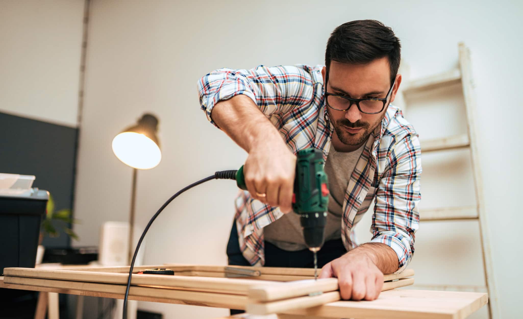 A Pro uses a power drill on a workbench next to an electric lamp.