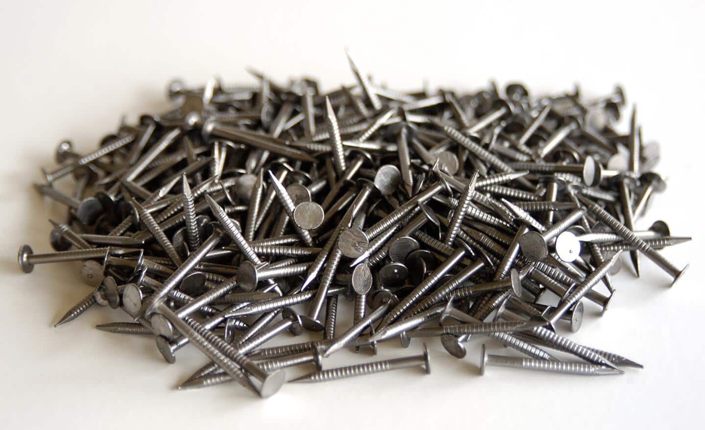A pile of drywall nails with ringed shanks placed on a white tabletop.
