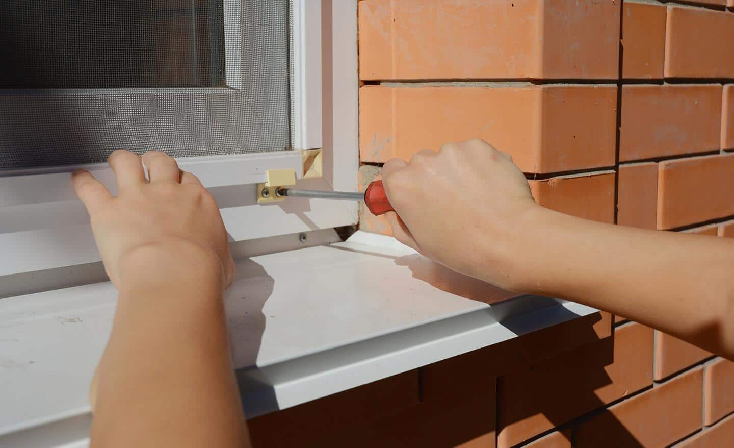 Someone installing a replacement screen on the outside of a window.