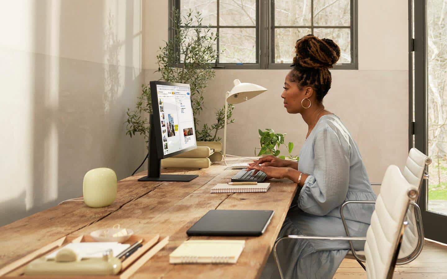 A woman uses a computer with a smart home speaker on the desk. A woman uses a computer with a smart home speaker on the desk.