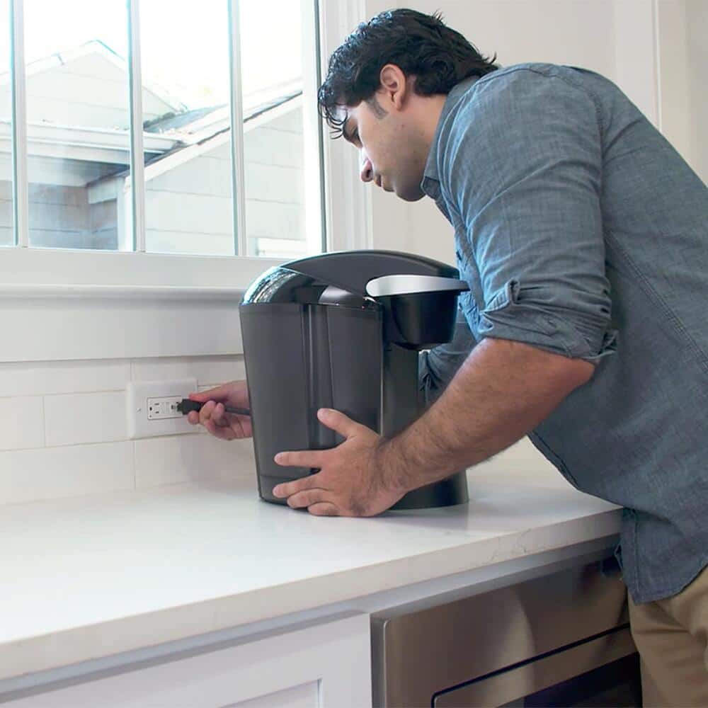 A man plugs a coffee maker into a kitchen GFCI receptacle.