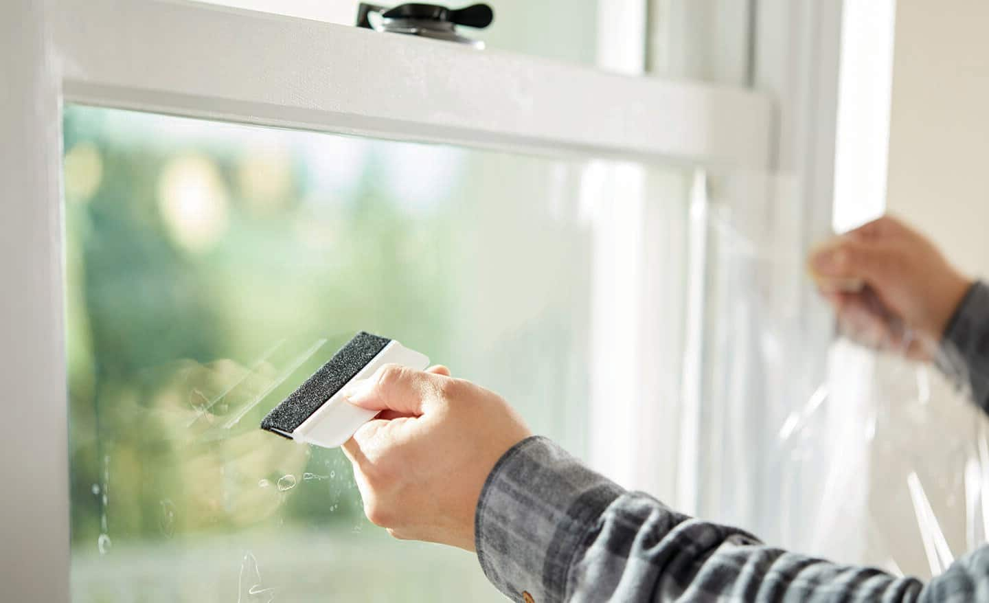 A person places window security film on a window.