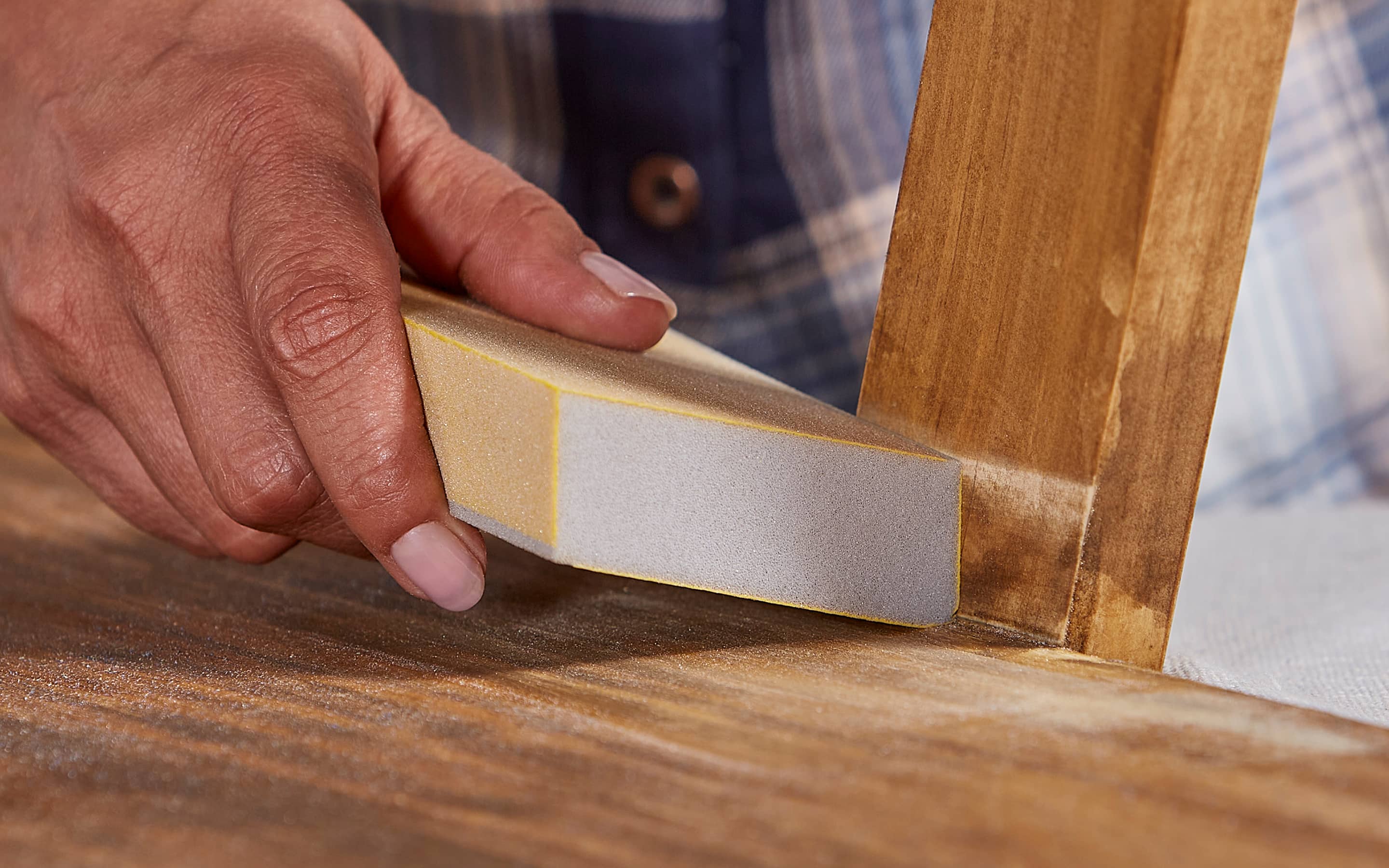 A person sands wood with a sanding block.