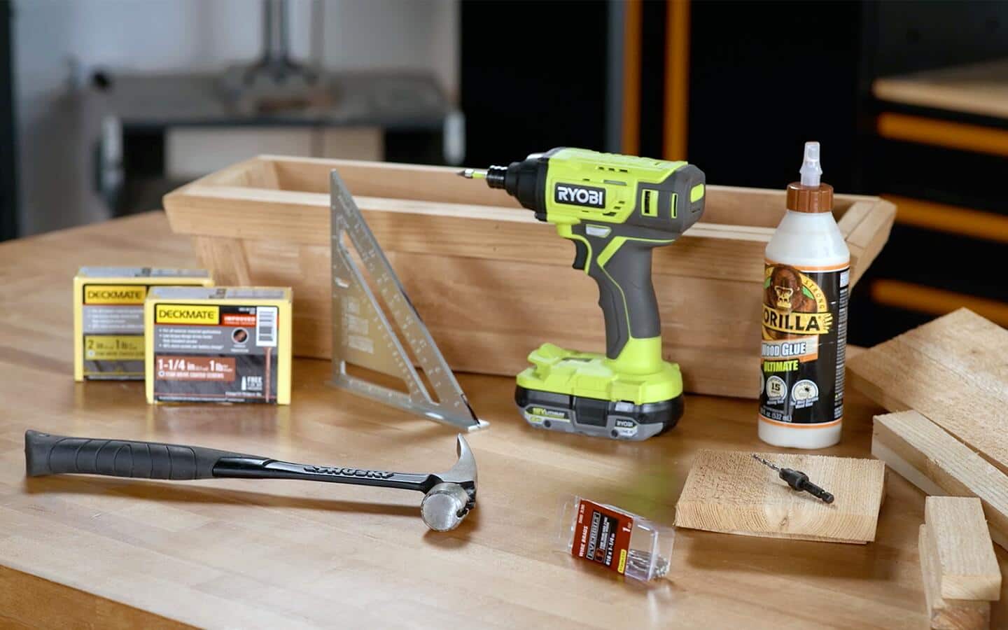 Assorted tools and materials for window box construction, including a power drill, on a wooden table.