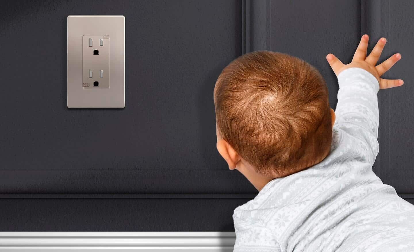 A baby crawling up to a tamper-resistant receptacle on a wall.