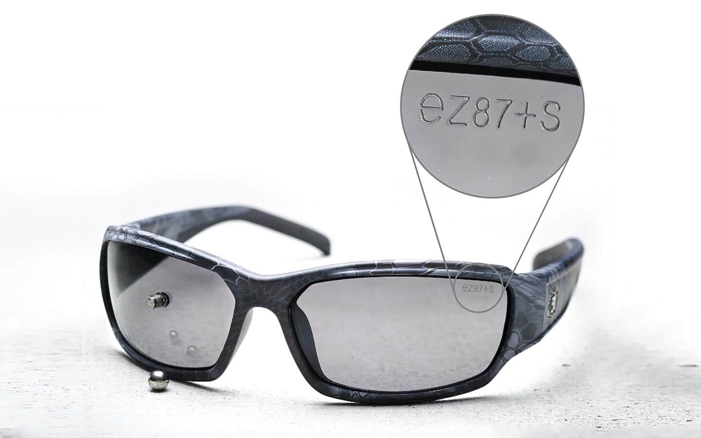 A pair of impact rated safety glasses with a callout showing the safety rating imprint. A pair of impact rated safety glasses with a callout showing the safety rating imprint.